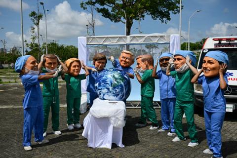 Oxfam activists wearing oversized masks pose during their "Big Heads" protest at Utinga Park in Belem in November 2025, to simulate a chaotic emergency room and highlight that as COP30 ends, the planet is in critical condition. 